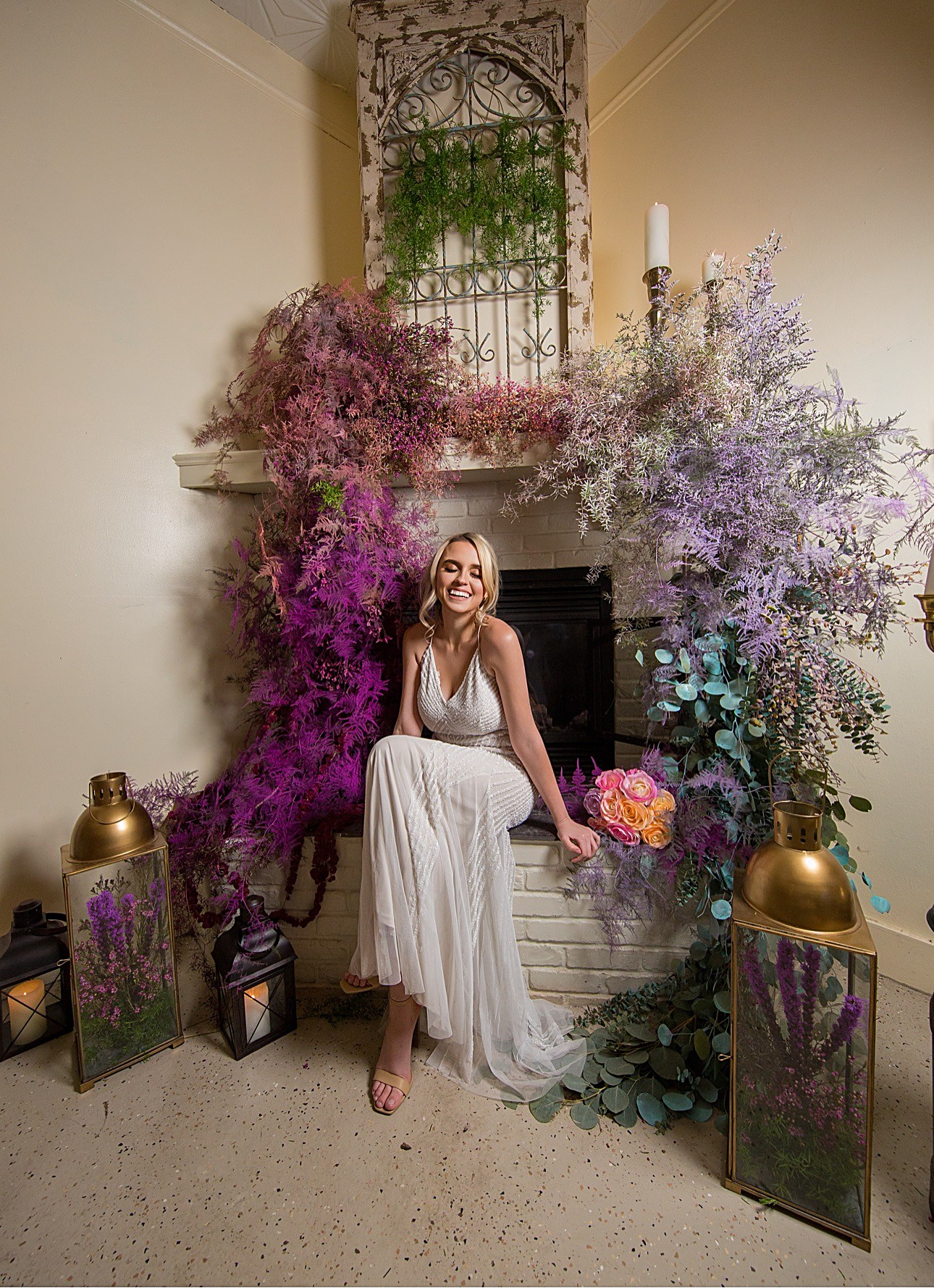 La novia sonriendo sentada junto a la chimenea, rodeada de flores moradas y lavanda